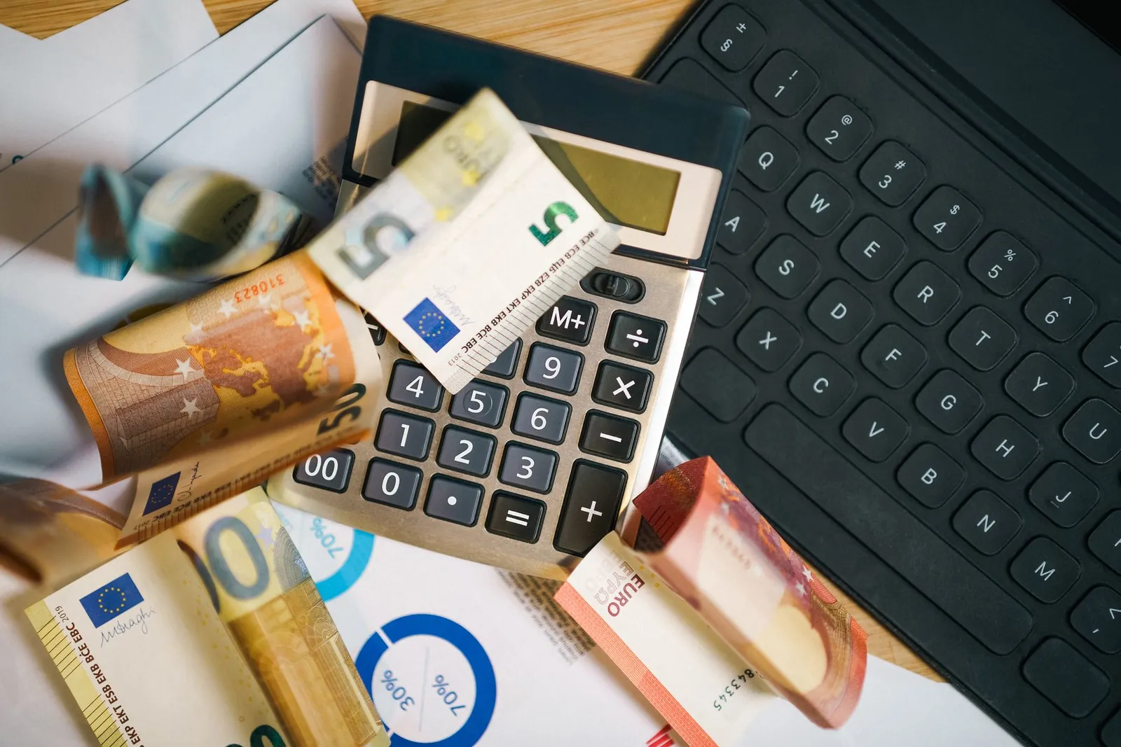 Calculatrice, billets en euros et documents chiffrés posés sur un bureau