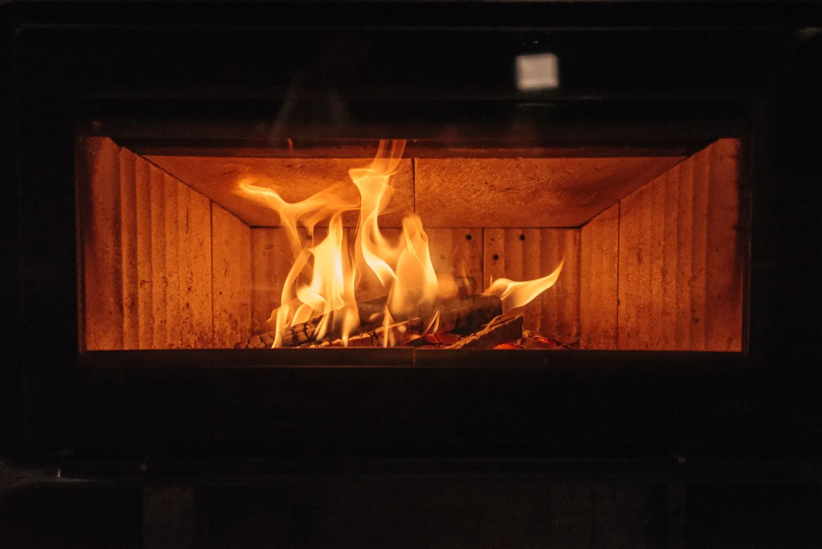 Flammes montant au-dessus du lit de bûches dans le foyer vitré d'un poêle à bois