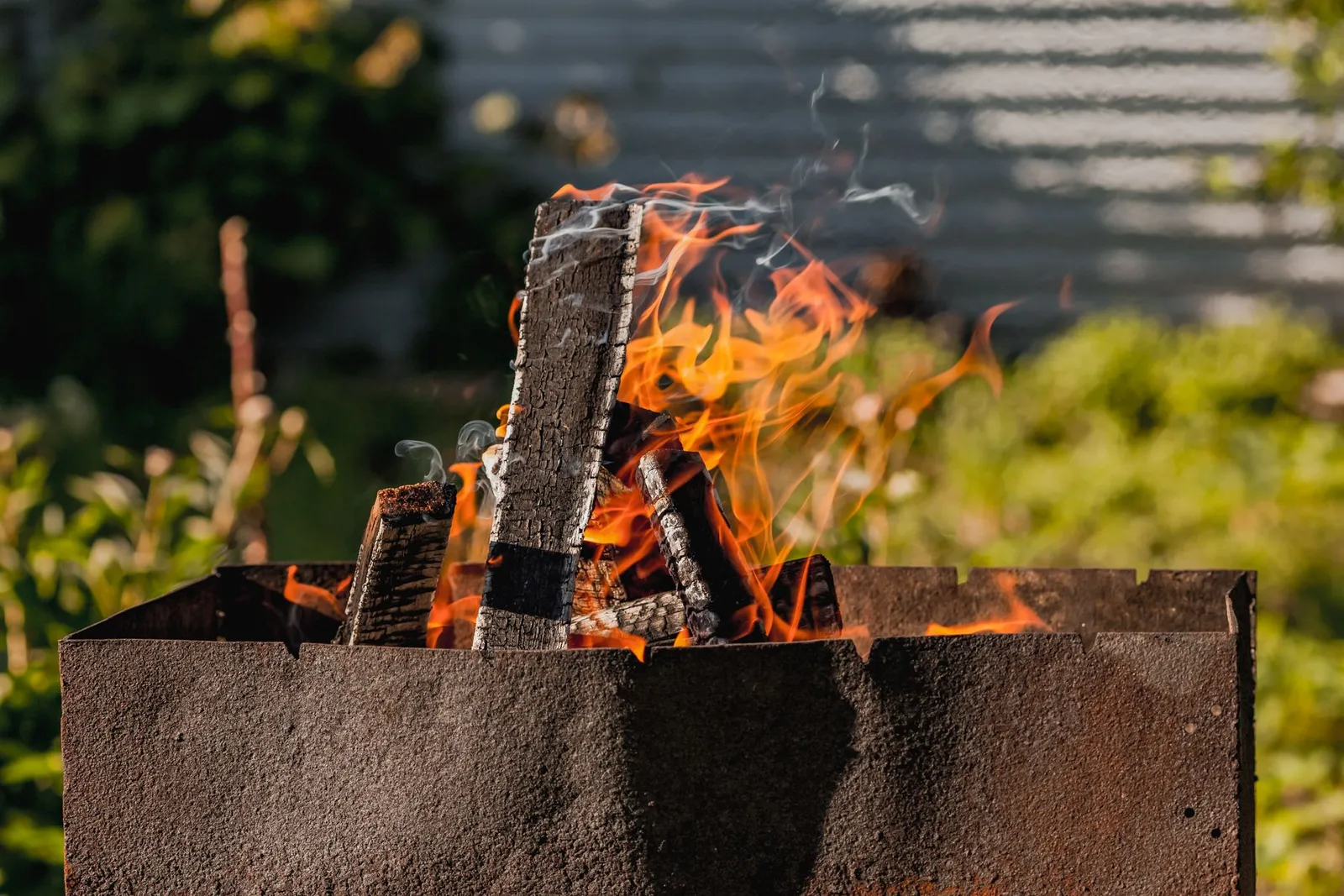 Bûches en train de flamber dans un brasero de jardin en acier, au fond d'un jardin