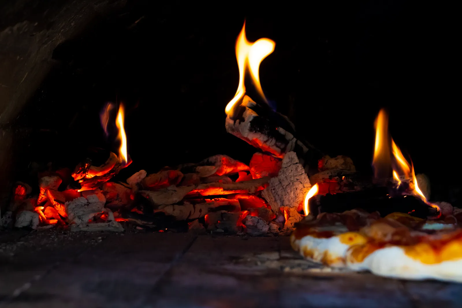 Flambée et braises au fond d'un four à pizza en briques, pizza en cuisson sur la sole
