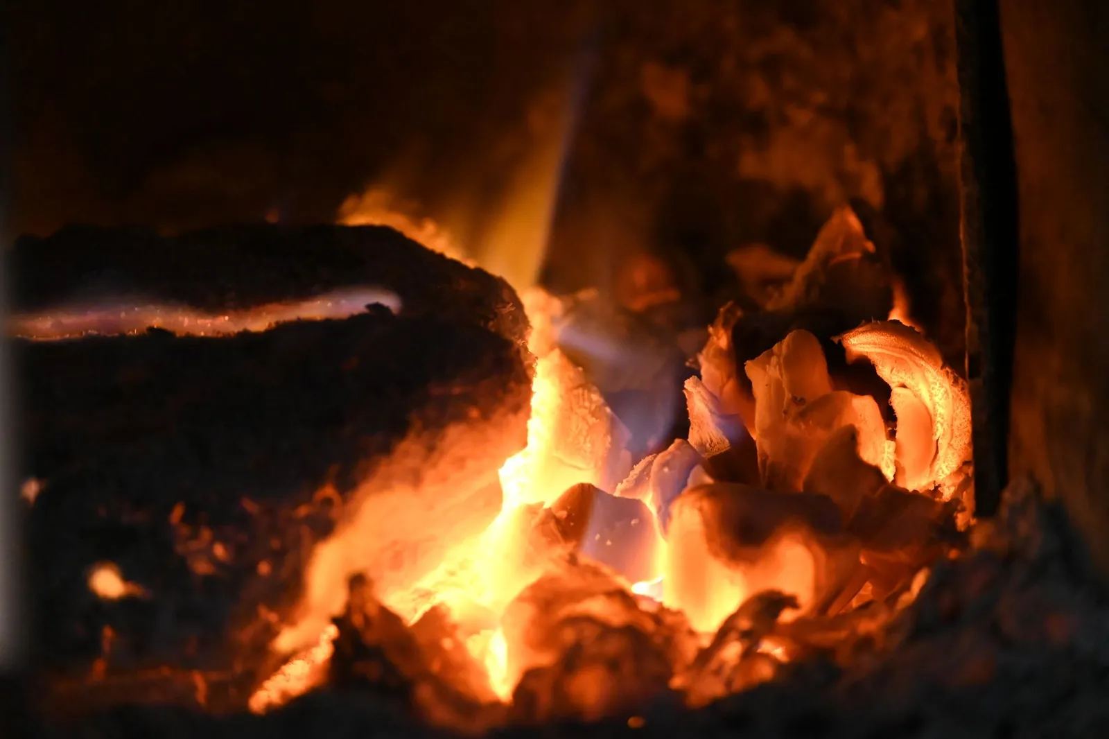 Lit de braises rougeoyantes et flammes basses sur une grosse bûche dans le foyer d'un poêle à bois