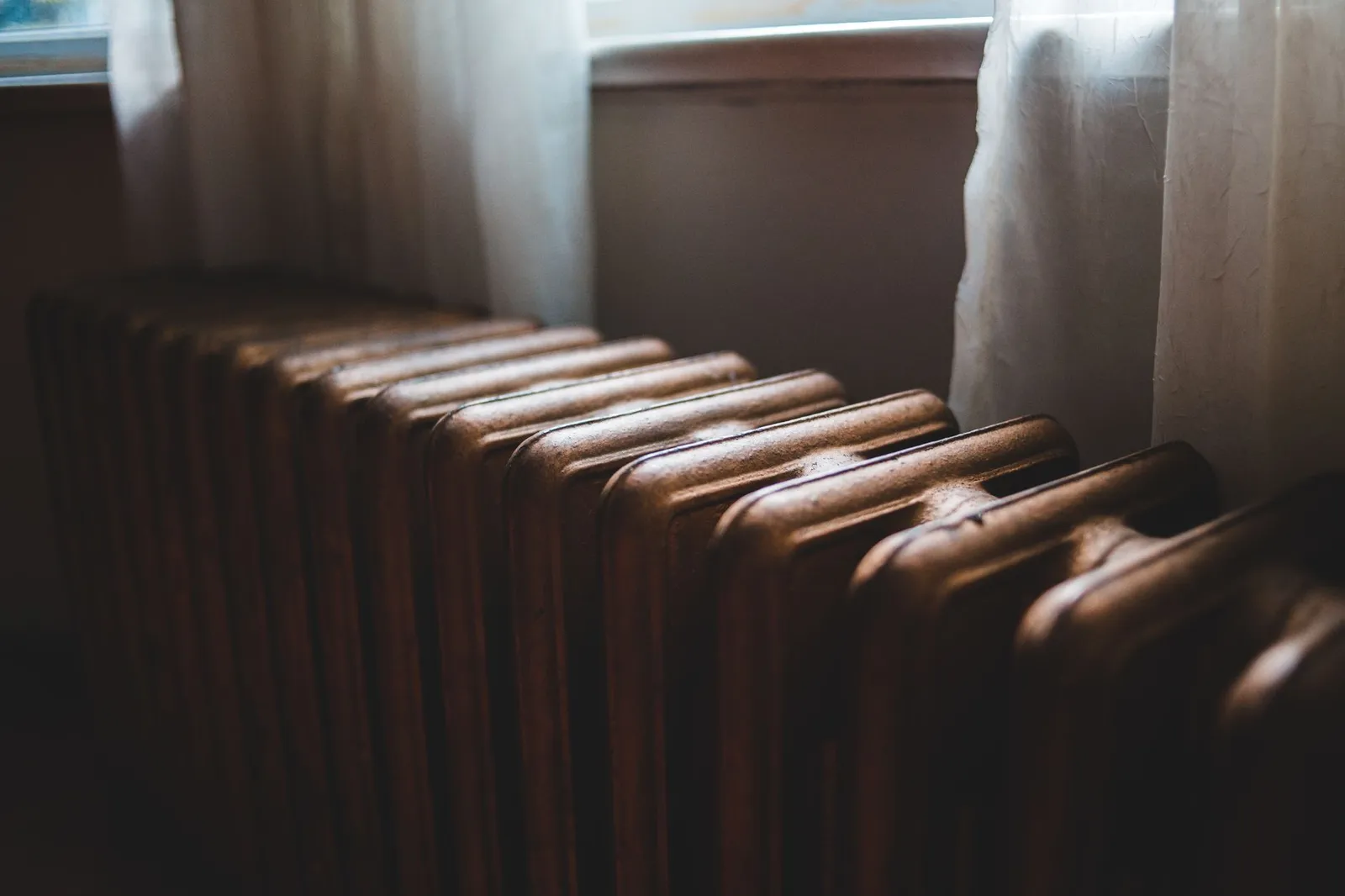 Radiateur en fonte sous une fenêtre, alimenté par un circuit de chauffage central au bois