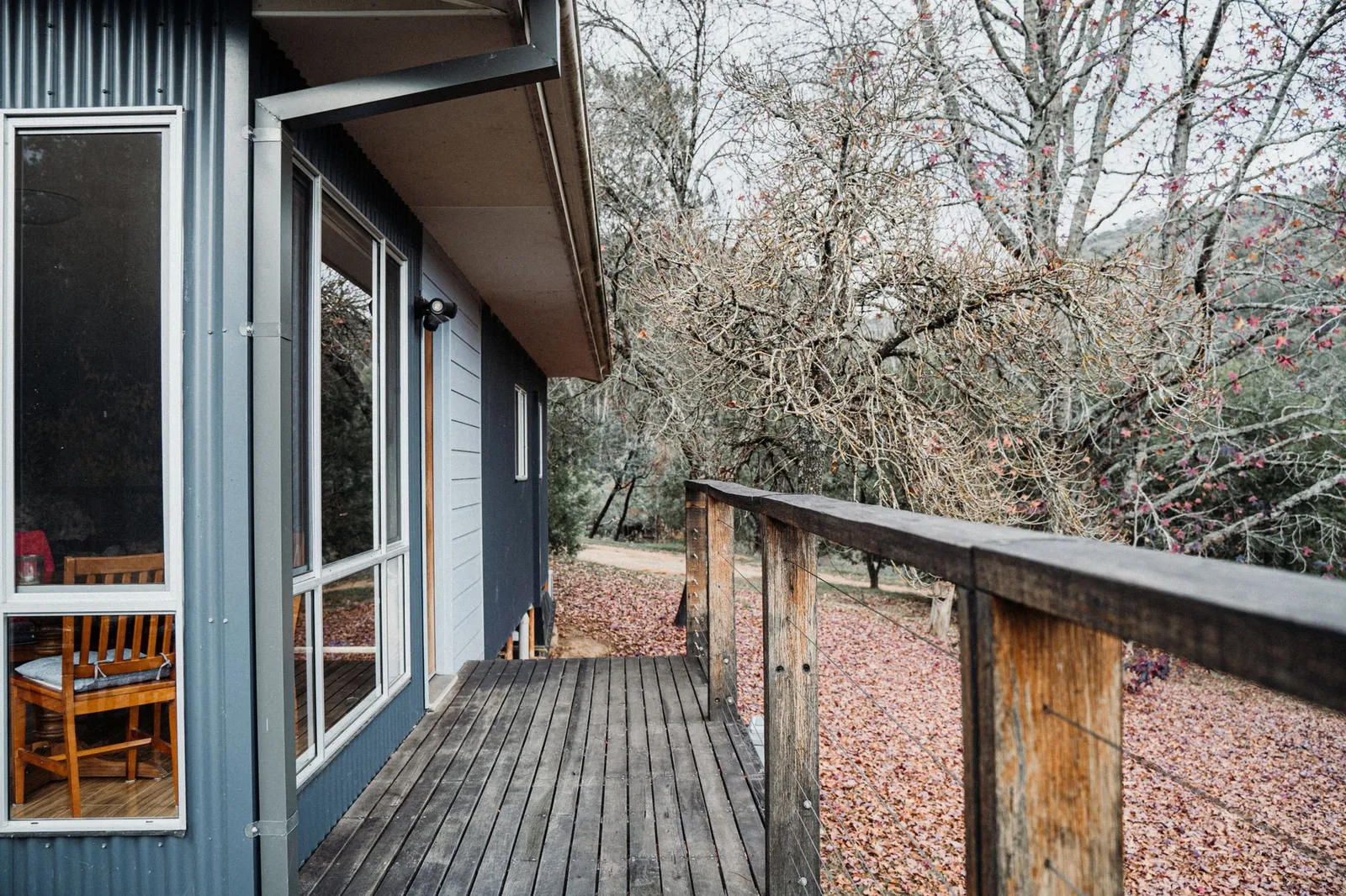 Terrasse en bois d'automne aux lames humides, feuilles mortes accumulées entre les joints