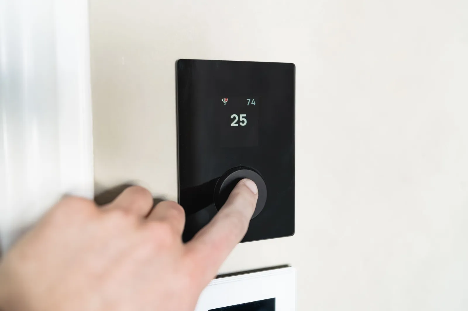 Main réglant un thermostat d'ambiance mural dans un intérieur clair